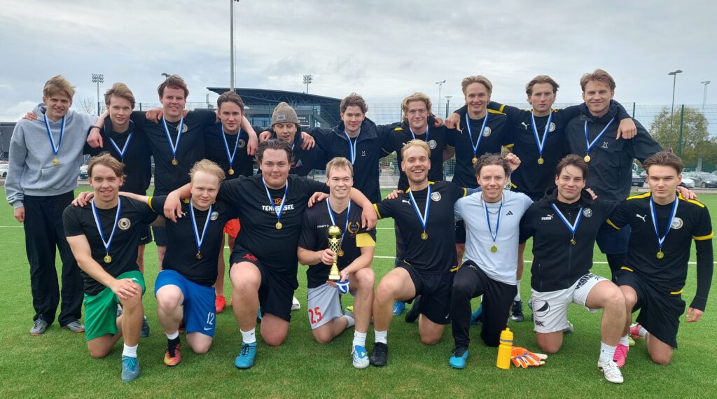 Jalkapallon harrastesarjan voittajajoukkue Henrik Street Athletics ryhmäkuvassa mitalit kaulassaan.